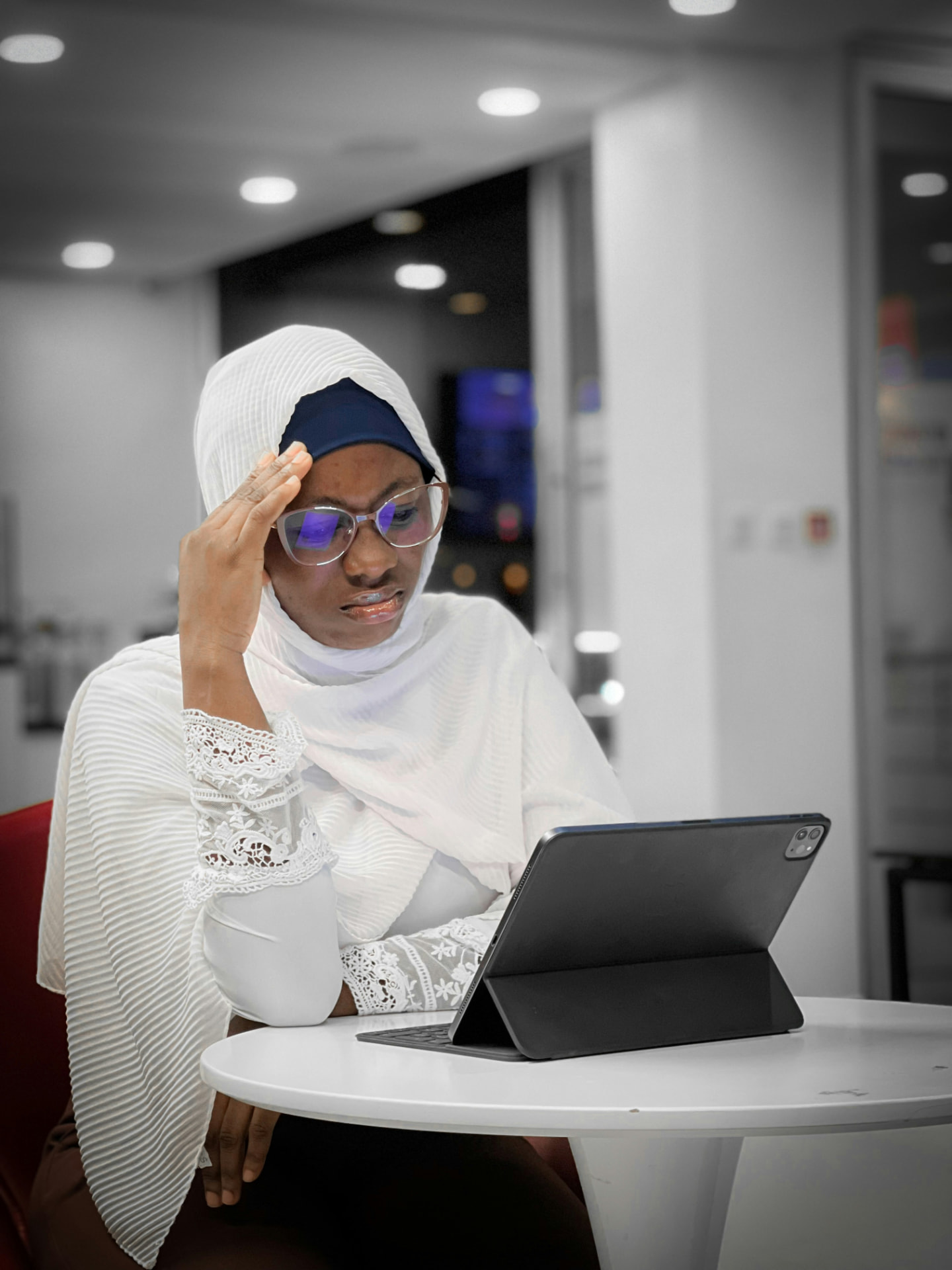 A woman in a hijab and glasses using a tablet in a modern office setting