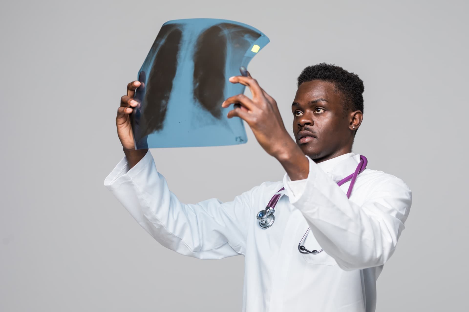 A doctor in a white coat holds up a chest X-ray film and examines it